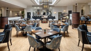 A spacious hotel lobby with multiple seating areas, a central bar, and a high ceiling with a geometric light fixture.