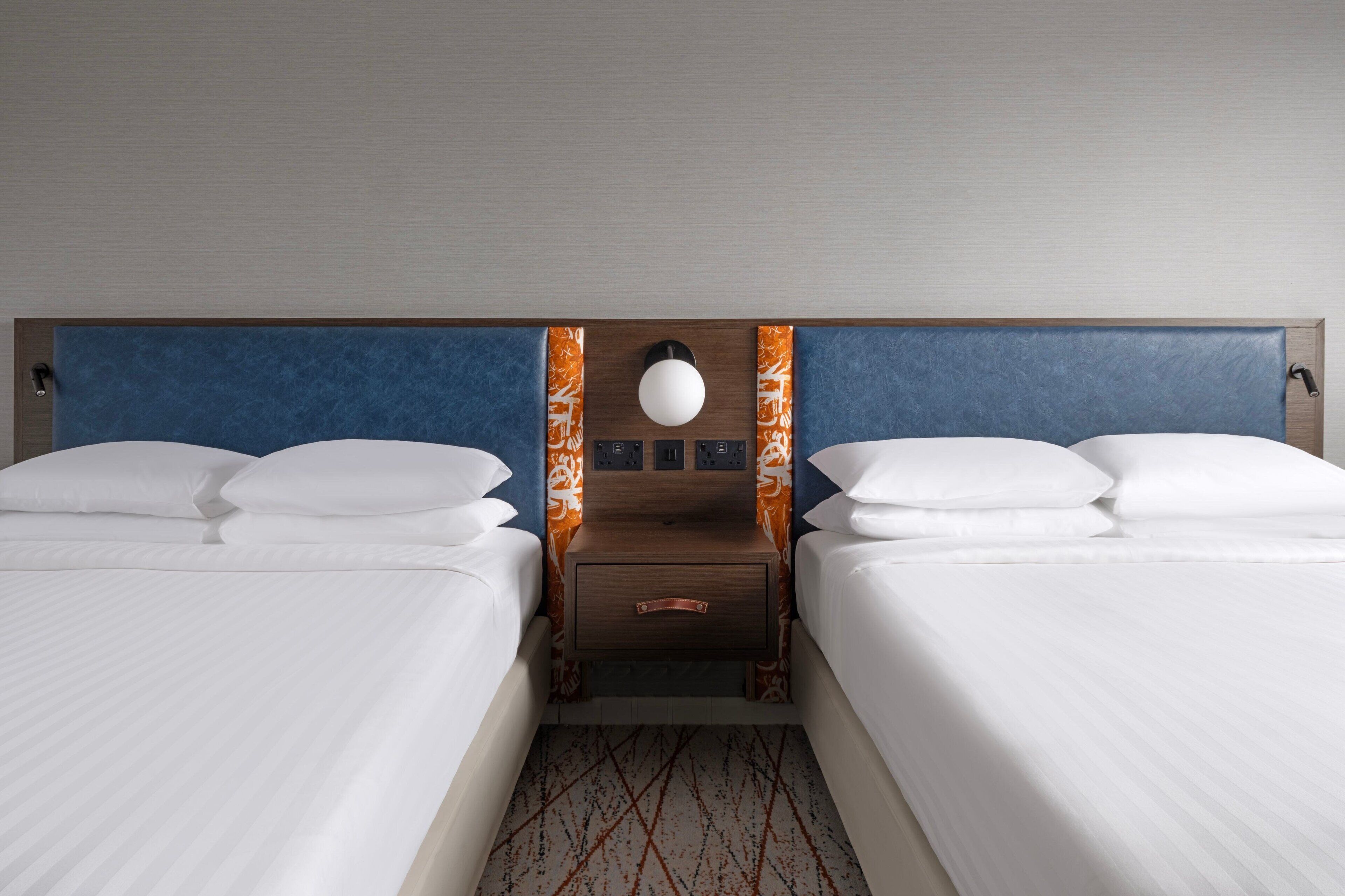 Ein Hotelzimmer mit zwei Betten, einem Nachttisch mit Lampe und einer Wandsteckdose.