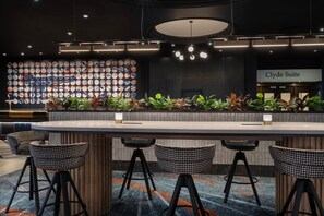A bar area with a long counter, black woven stools, and a wall of sports-themed plates. - Glasgow Marriott Hotel (Glasgow)