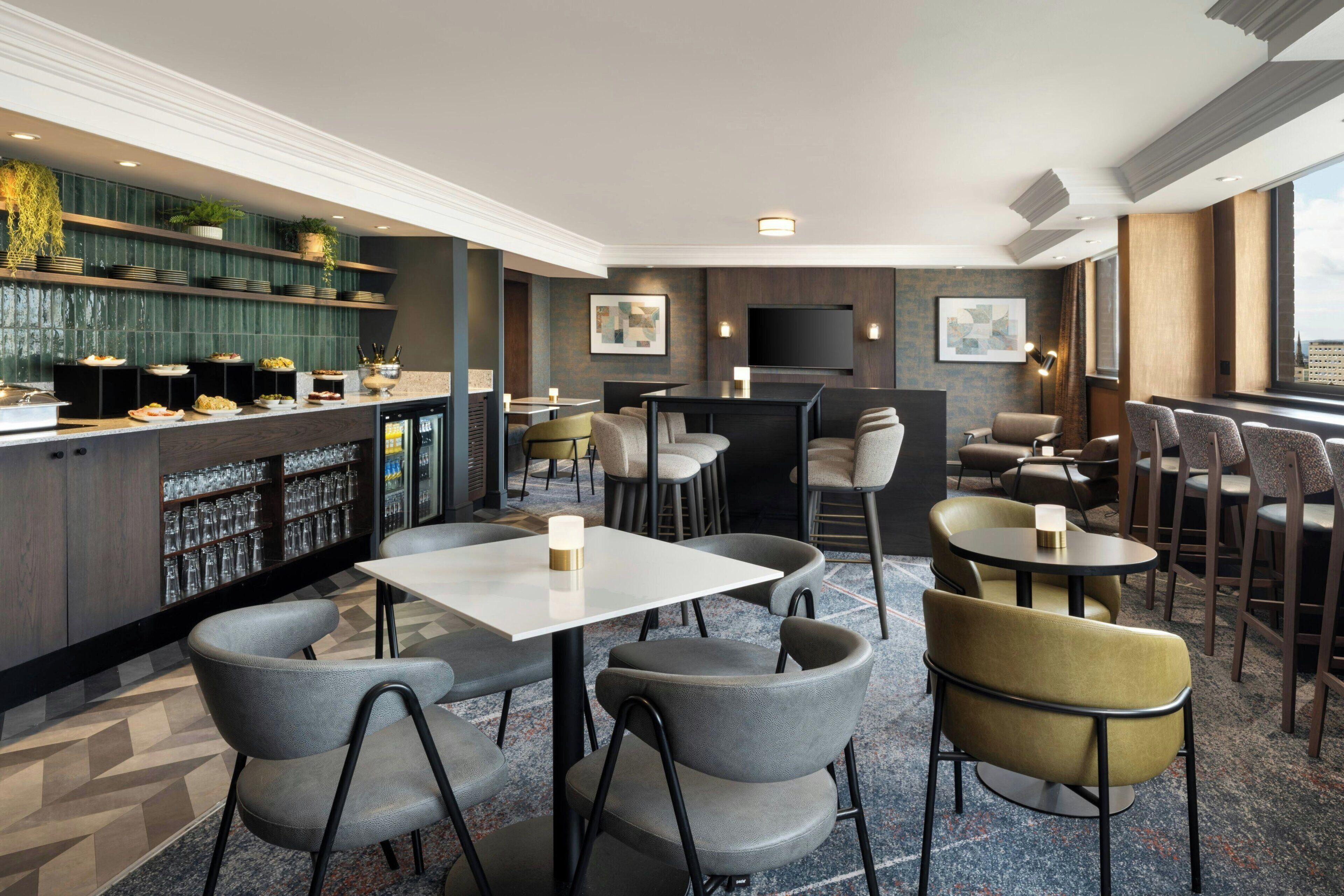 Een moderne hotel lobby met een bar, zitgedeeltes en een groot televisiescherm.