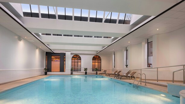 An indoor swimming pool with clear blue water, a skylight ceiling, and lounge chairs along the side.