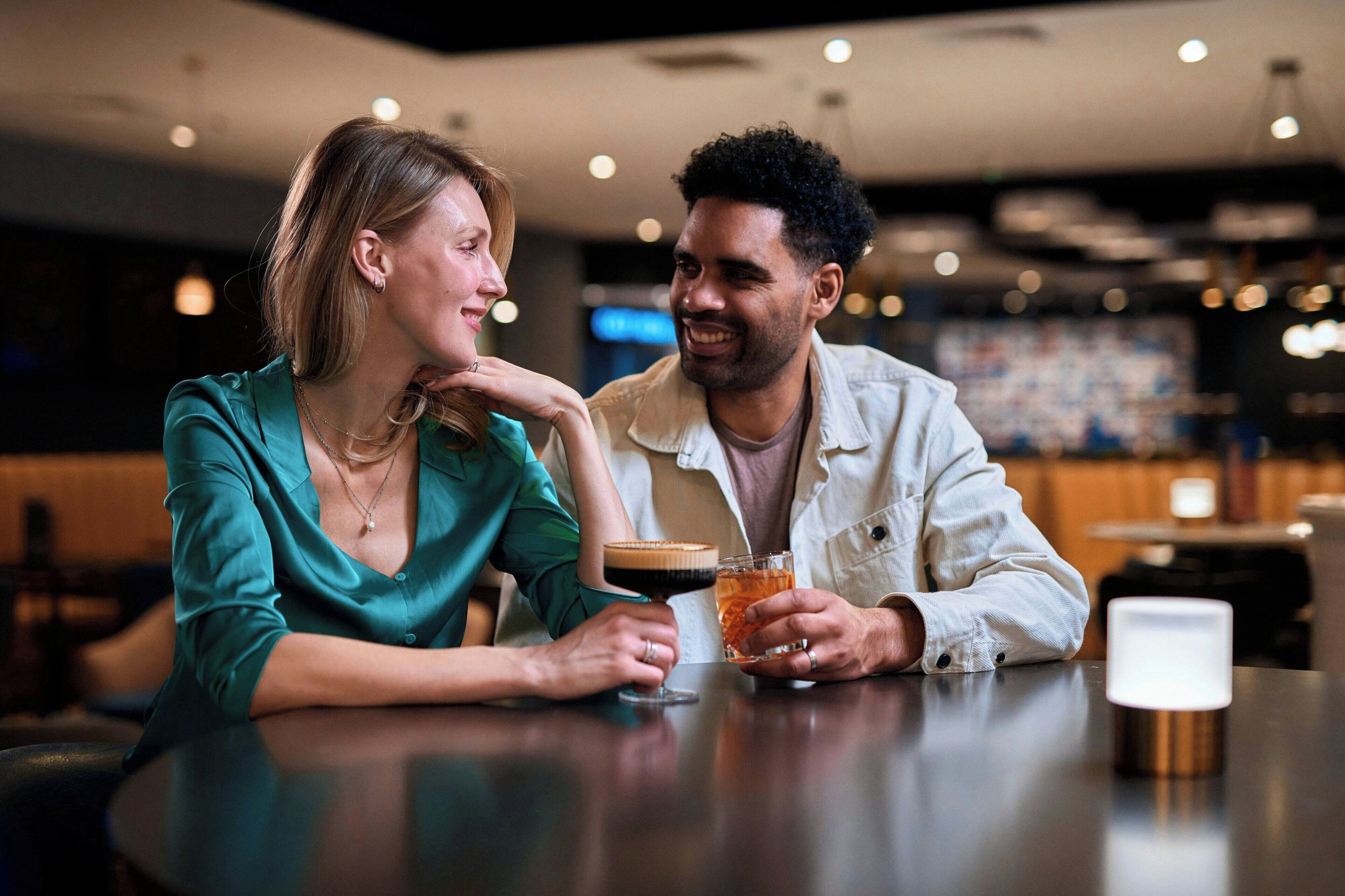 Two people sitting at a table in a dimly lit indoor setting, possibly a restaurant or cafe.