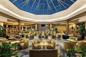 A spacious lobby with a central seating area, a bar, and a ceiling with a geometric glass design. - Paris Marriott Charles de Gaulle Airport Hotel (Roissy-en-France)