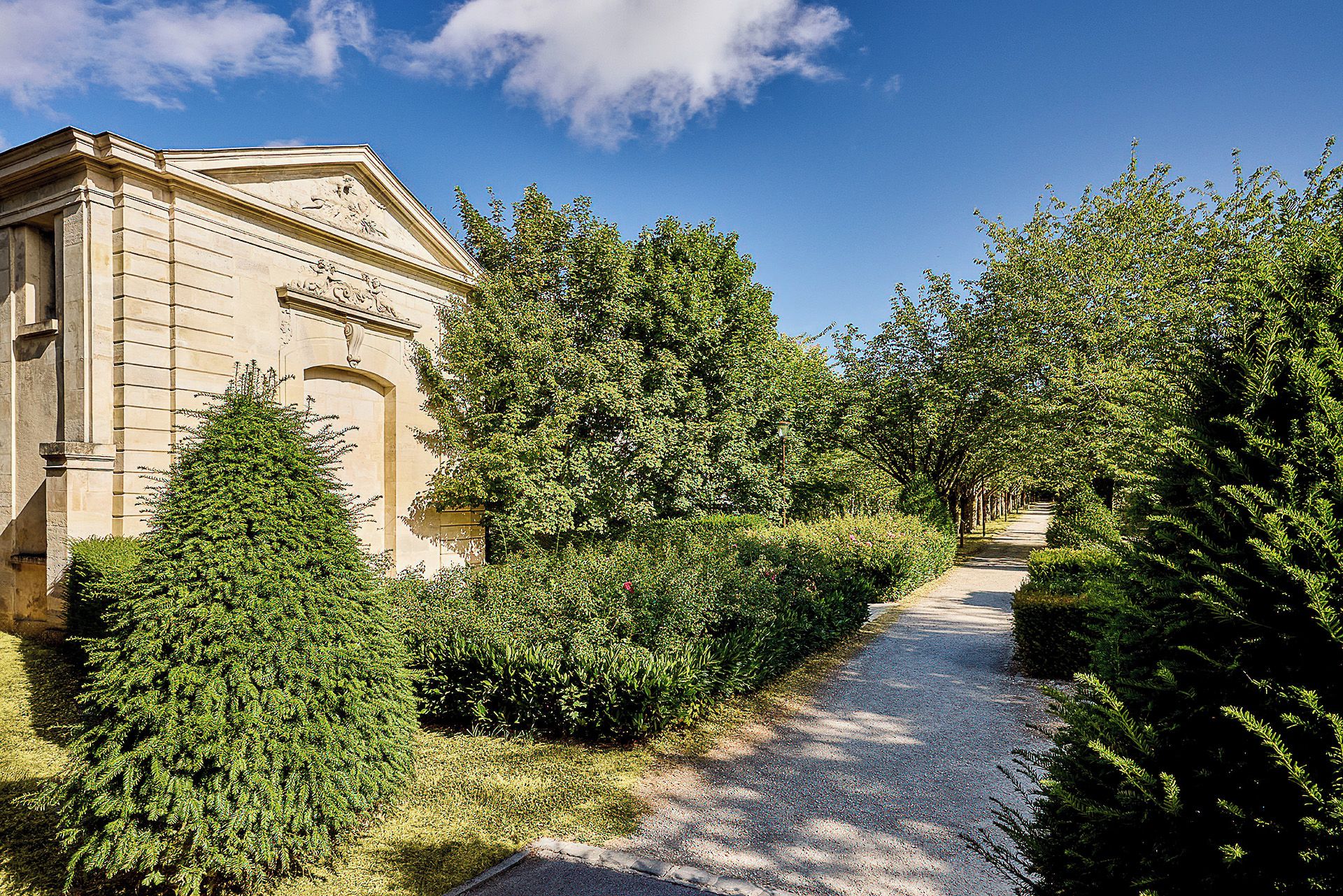 Un sentier bordé d’une végétation luxuriante et un bâtiment classique doté de colonnes.