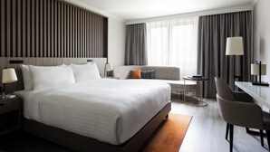 A modern hotel room with a large bed, a sofa, a desk, and a lamp. - Paris Marriott Charles de Gaulle Airport Hotel (Roissy-en-France)