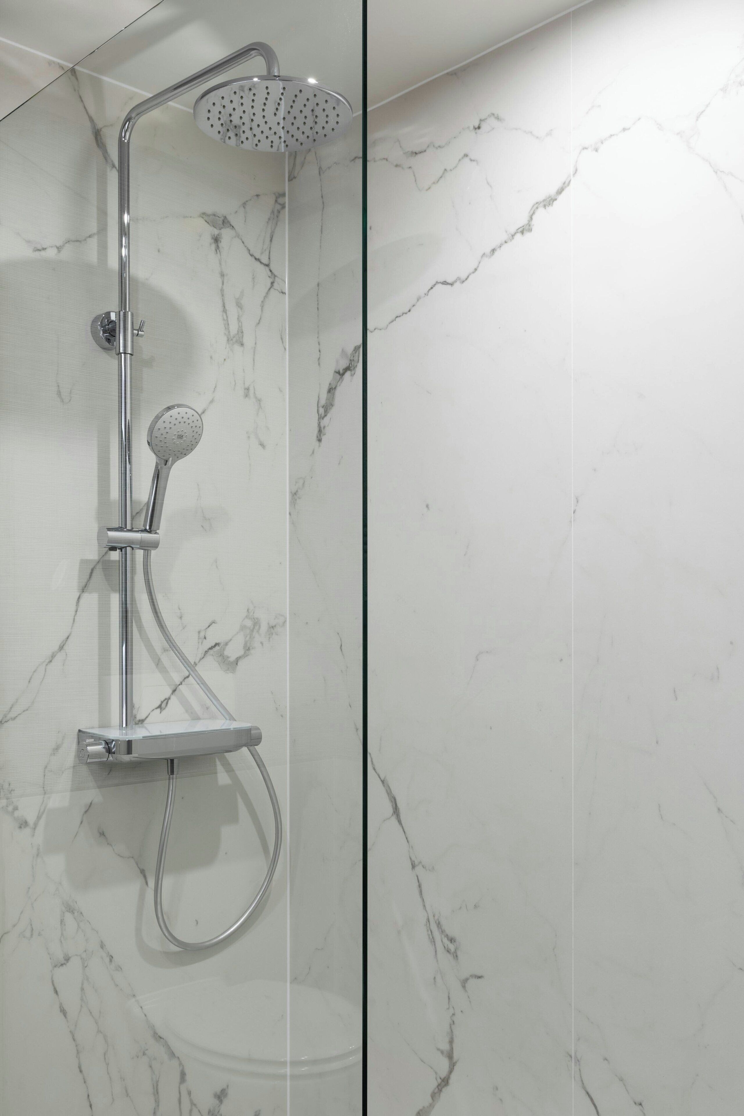 A modern bathroom with a shower, marble walls, and a glass partition.