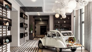 A vintage car parked in a modern hotel lobby with patterned flooring, shelves with decorative items, and hanging light fixtures. - Paris Marriott Charles de Gaulle Airport Hotel (Roissy-en-France)