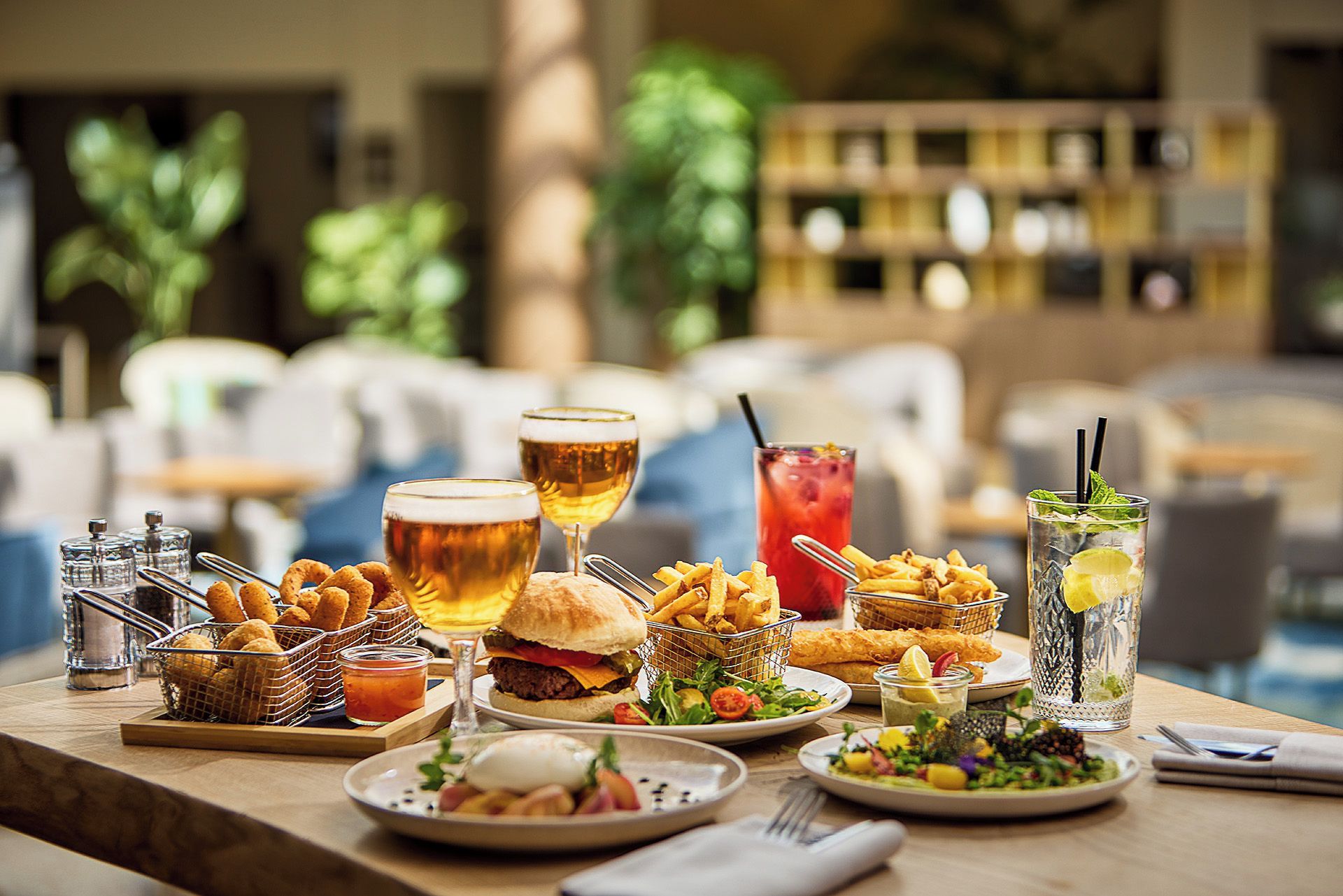 A dining table with various food items and drinks, including a burger, fries, and a salad.