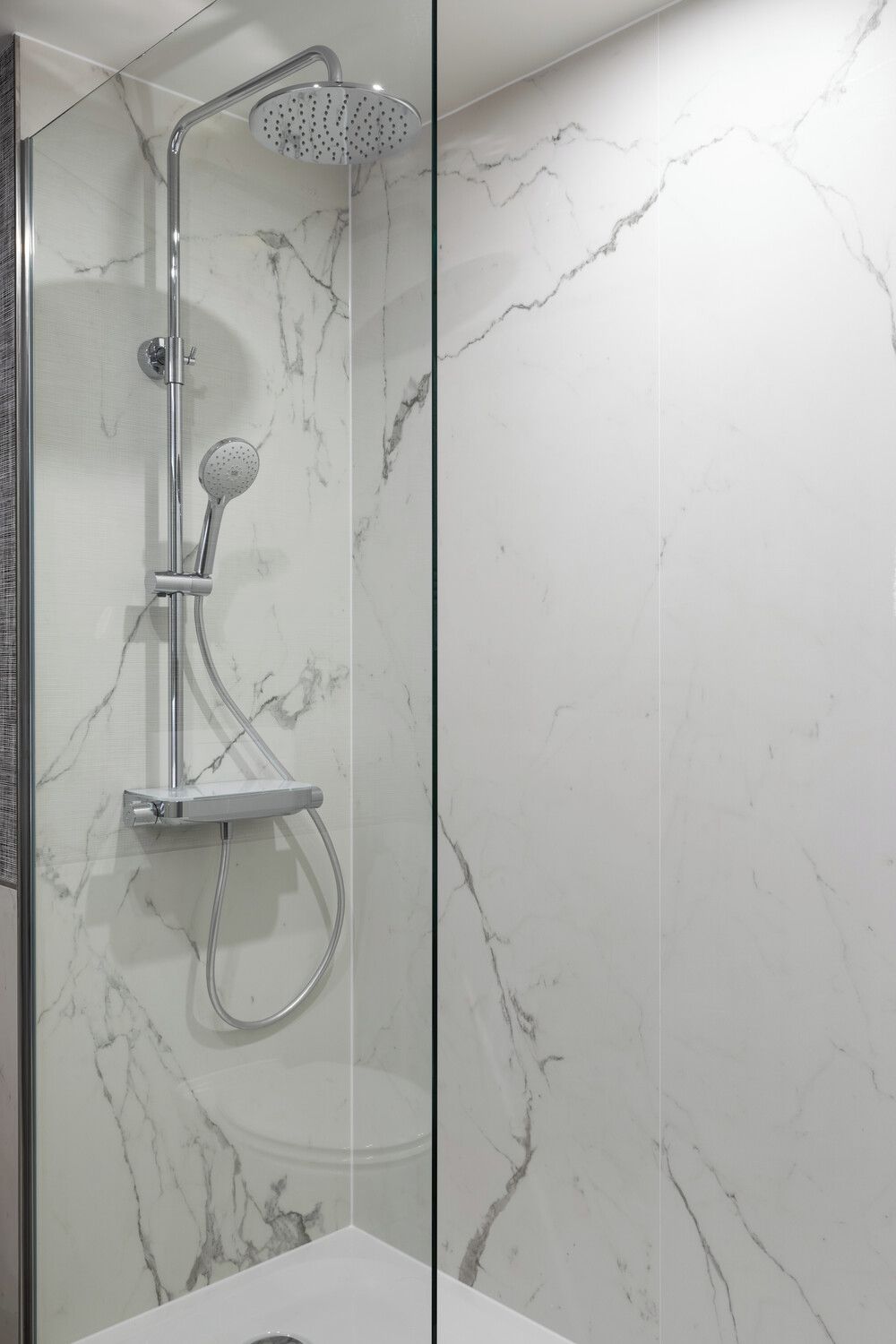 Un baño moderno con ducha de vidrio, paredes de mármol y un lavamanos blanco.