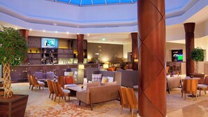 A spacious lobby with a high ceiling and a skylight, featuring comfortable seating areas, a bar, and a television screen. - Paris Marriott Charles de Gaulle Airport Hotel (Roissy-en-France)