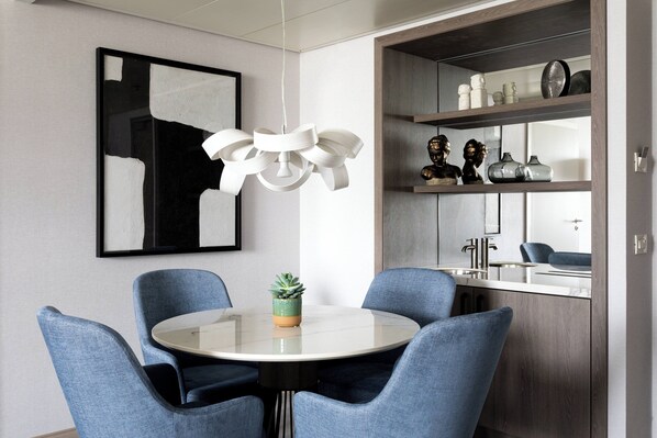 Un comedor moderno con una mesa redonda, sillas tapizadas en azul, una lámpara colgante blanca y una planta en maceta.