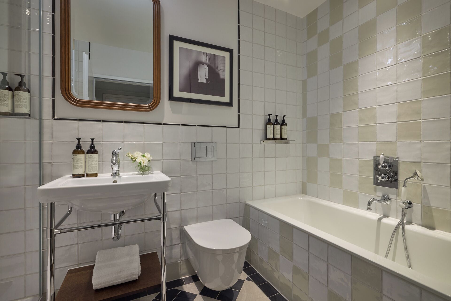 A bathroom with a white sink, a toilet, a bathtub, and a shower. There are toiletries on the sink and a framed picture on the wall.