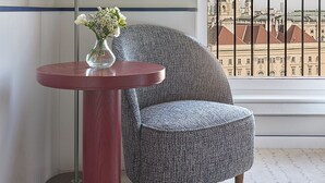 Une pièce comprenant une table ronde, une chaise, un lampadaire et une grande fenêtre donnant sur un paysage urbain.