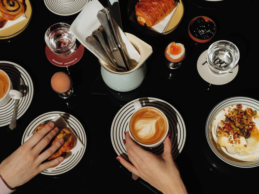 A table with plates of food and drinks, including pastries, coffee, and a dessert with nuts.