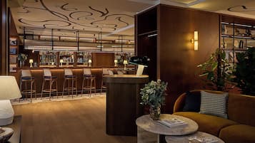 Uma área de bar com banquetas, balcão e adega repleta de garrafas. Há também um espaço de estar com sofá e mesa de centro.