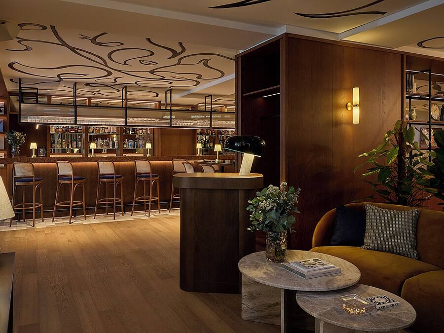 Uma área de bar com banquetas, balcão e adega repleta de garrafas. Há também um espaço de estar com sofá e mesa de centro.