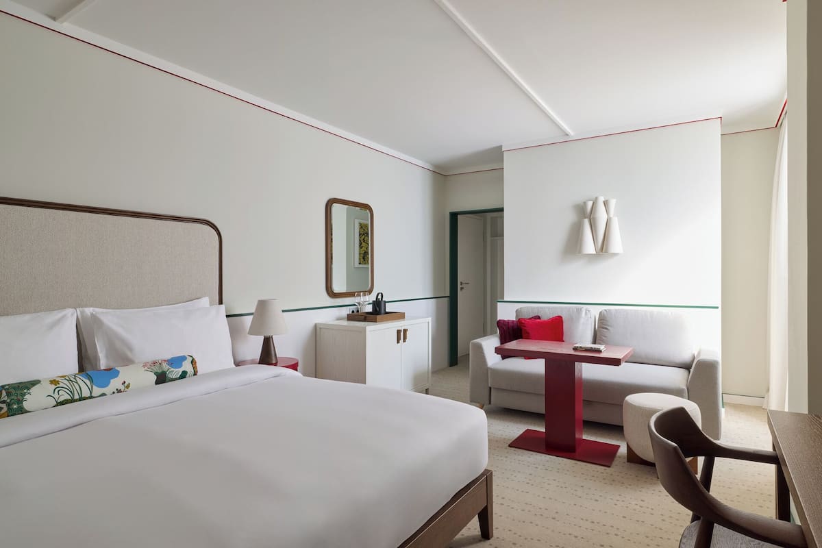 Una habitación de hotel con cama, escritorio, silla, sofá, espejo y una lámpara fijada en la pared.