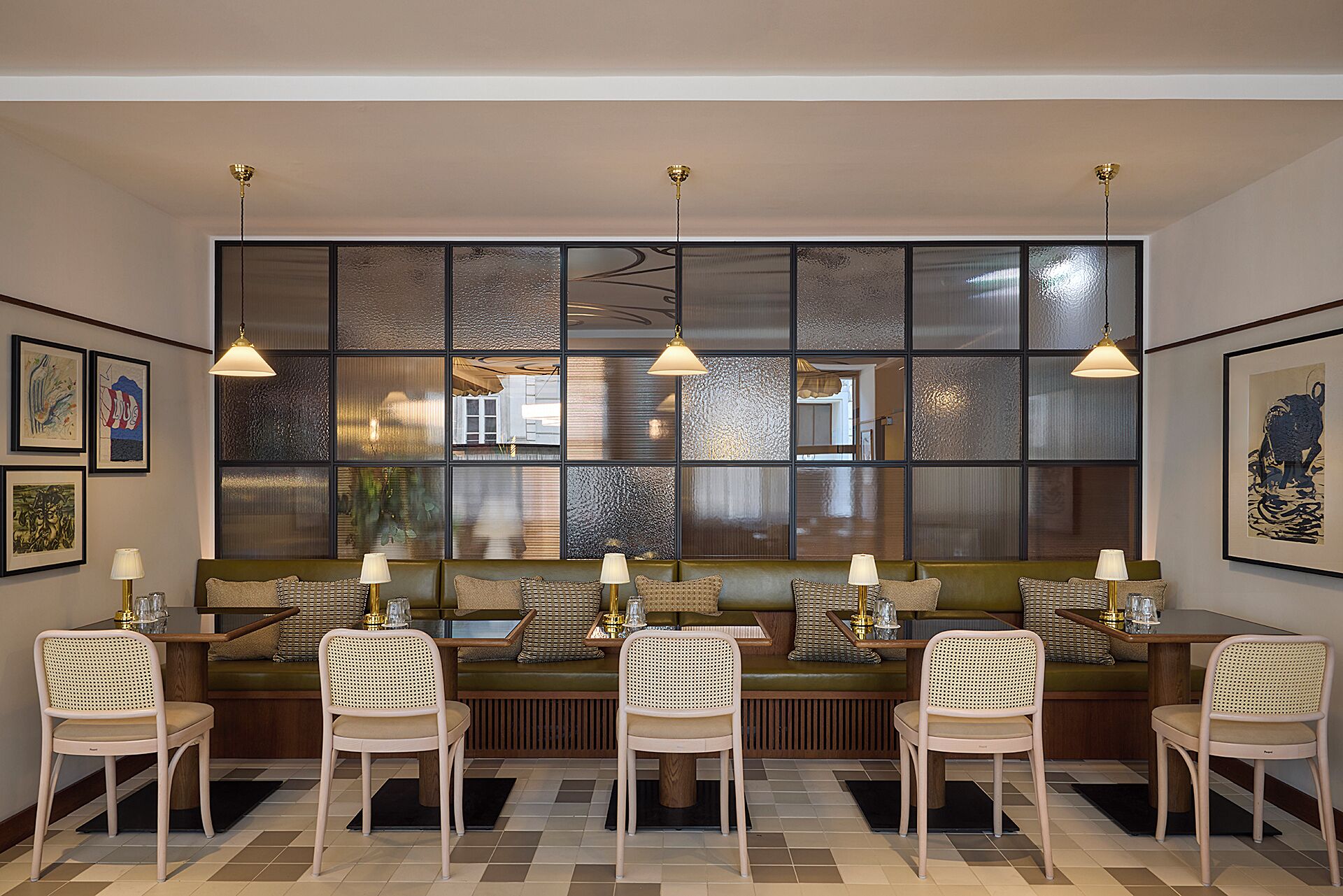 A dining area with a low, green upholstered bench and six chairs, a large window with textured glass panels, and three pendant lights.