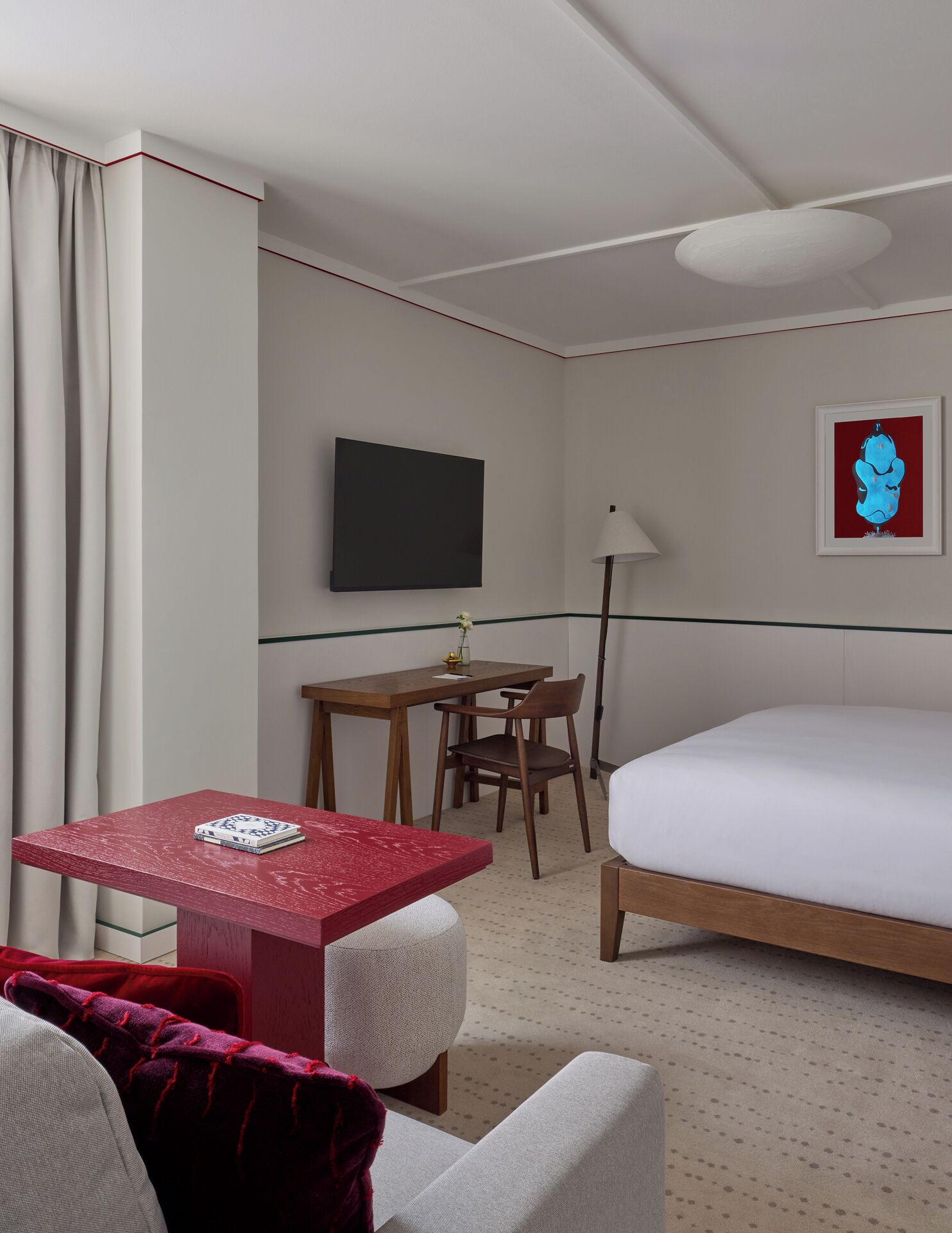 Quarto de hotel com cama, escrivaninha, cadeira, televisão e quadro na parede.