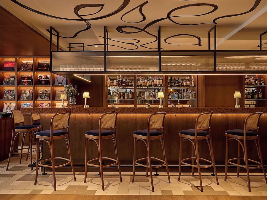 A bar area with wooden bar stools, a well-stocked liquor shelf, and framed pictures on the wall.