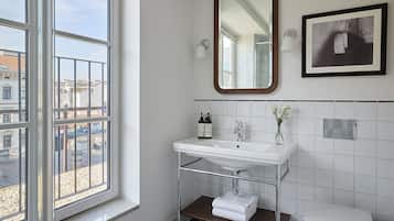 Een badkamer met een raam, een wastafel, een spiegel en een toilet.