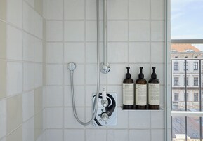 Casa de banho com chuveiro, janela e três frascos de champô Santal 33.