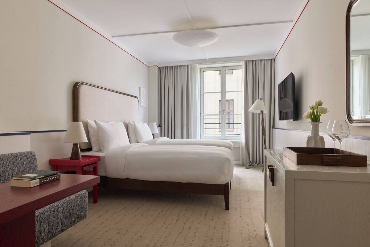 Habitación de hotel con cama, mesitas de noche, escritorio, silla, televisor y ventana con cortinas.