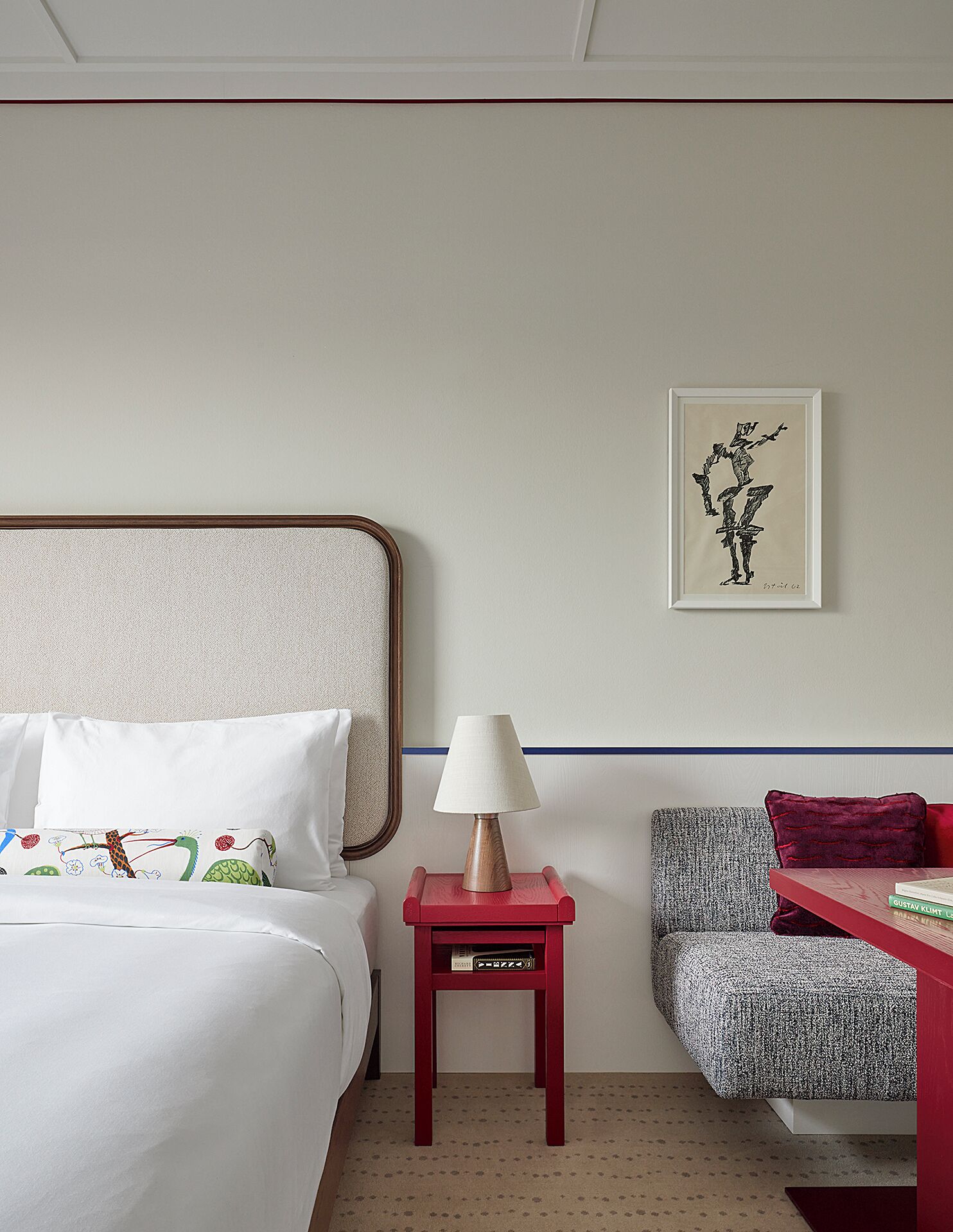 Una habitación de hotel con una cama, una mesita de noche con lámpara, una obra de arte enmarcada y un sillón estampado.