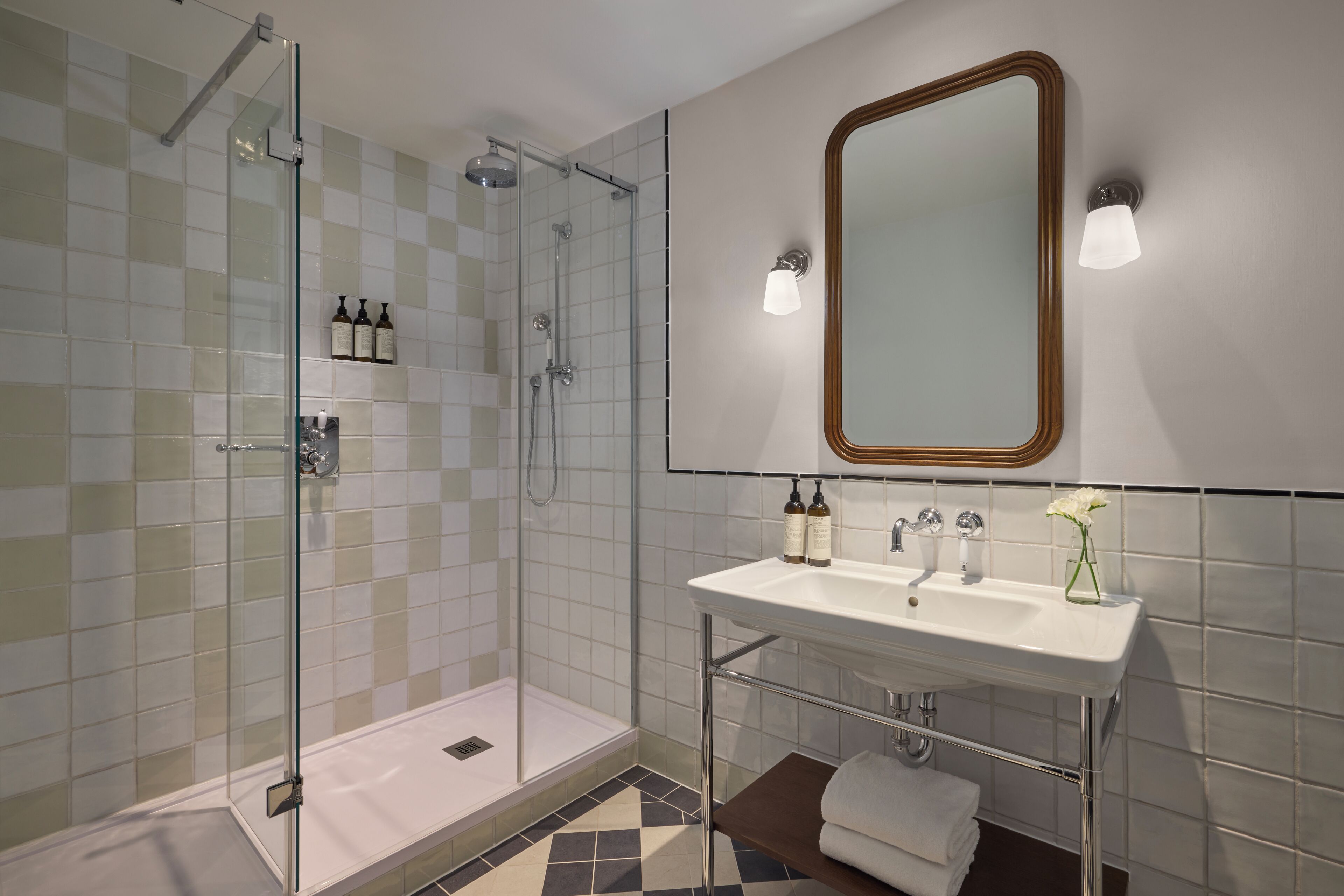 A modern bathroom with a glass shower enclosure, a white sink with a mirror above it, and a tiled floor.