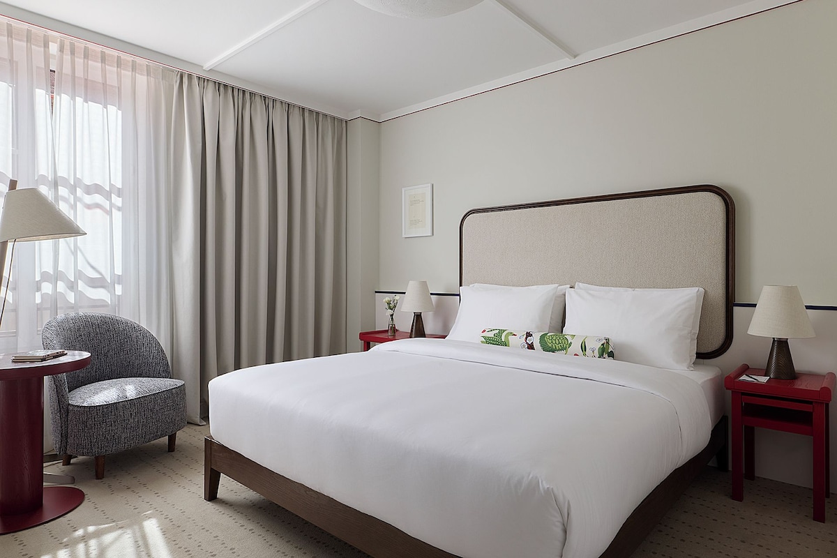 A hotel room with a large bed, two bedside tables, a chair, and a window with curtains.