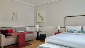Ein Hotelzimmer mit Bett, Sofa, kleinem Tisch, Nachttisch, Lampe, einem Bild an der Wand und einer Stehlampe.