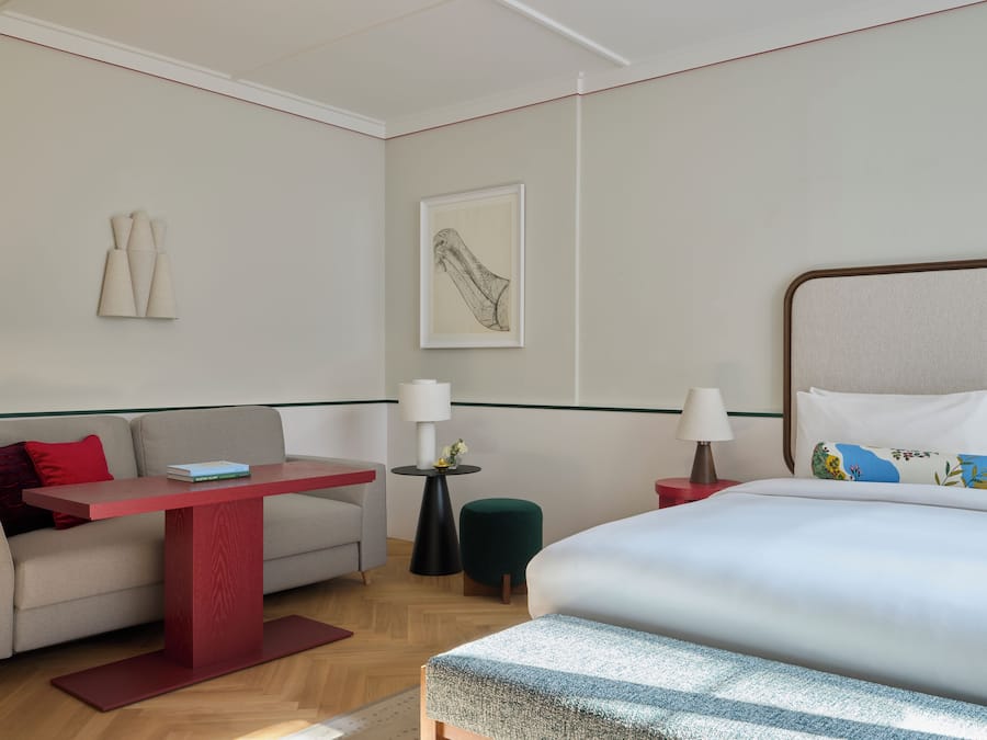 Ein Hotelzimmer mit Bett, Sofa, kleinem Tisch, Nachttisch, Lampe, einem Bild an der Wand und einer Stehlampe.
