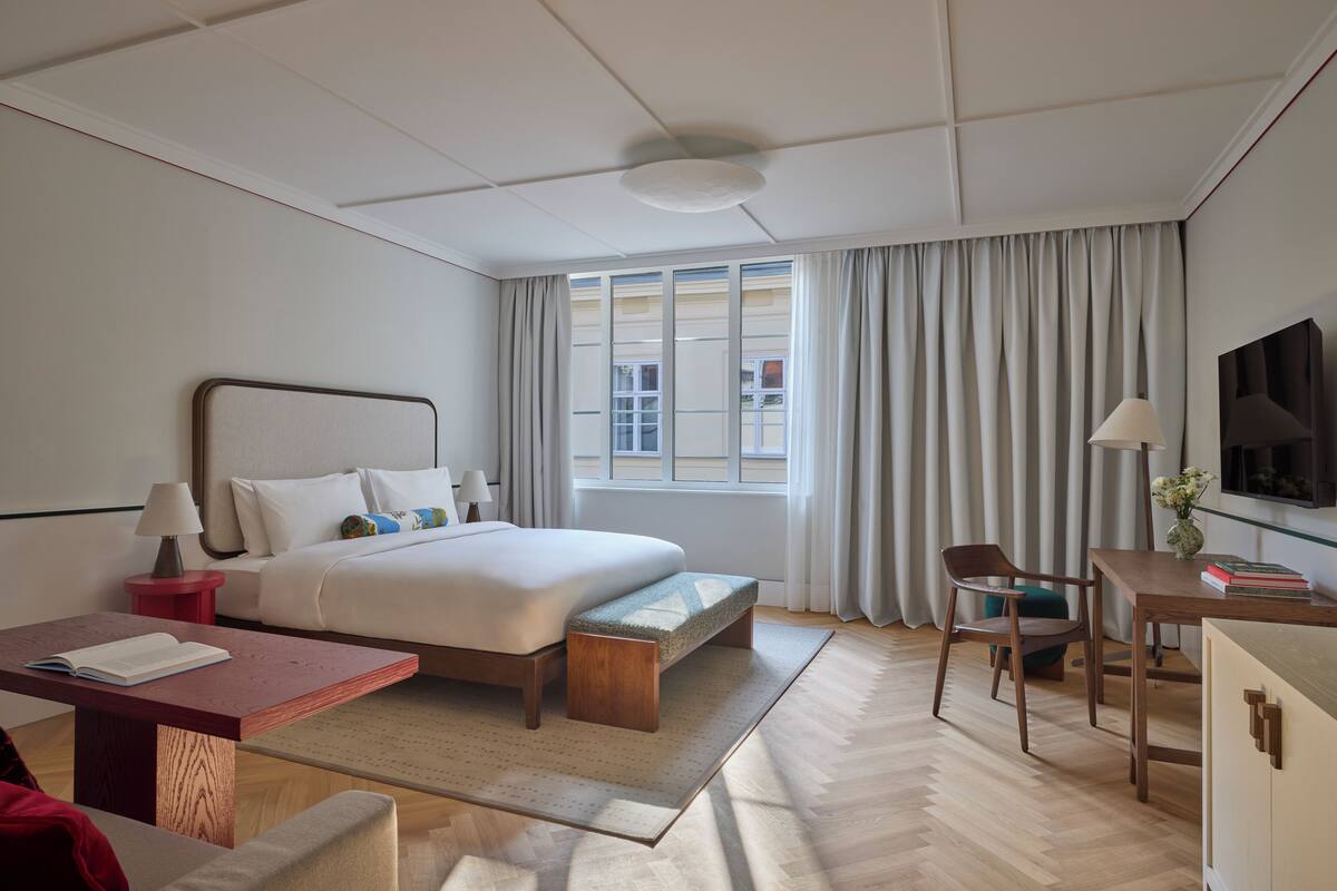 Habitación de hotel con cama, mesitas de noche, escritorio, silla, televisor y ventana con cortinas.