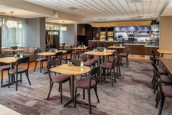Un hall d’hôtel doté de plusieurs espaces salon, d’un bar et d’une cuisine ouverte.