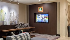 A modern hotel lobby with a seating area, a large screen displaying information, and a Starbucks logo on the wall.