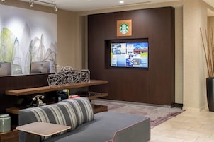 Un hall d’hôtel moderne avec un espace salon, un grand écran affichant des informations et le logo de Starbucks sur le mur.