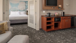 A hotel room with a bed, a sofa, a kitchenette, and a TV.