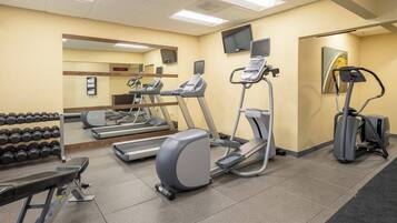 A gym with treadmills, elliptical machines, a bench press, and dumbbells.