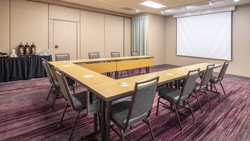 A conference room with a long table, chairs, a projector screen, and a carpeted floor.