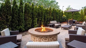 A patio area with a stone fire pit, wicker furniture, and a hedge in the background.