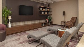 A modern living room with a flat-screen TV, built-in shelves, a brown leather armchair, and grey upholstered seating.