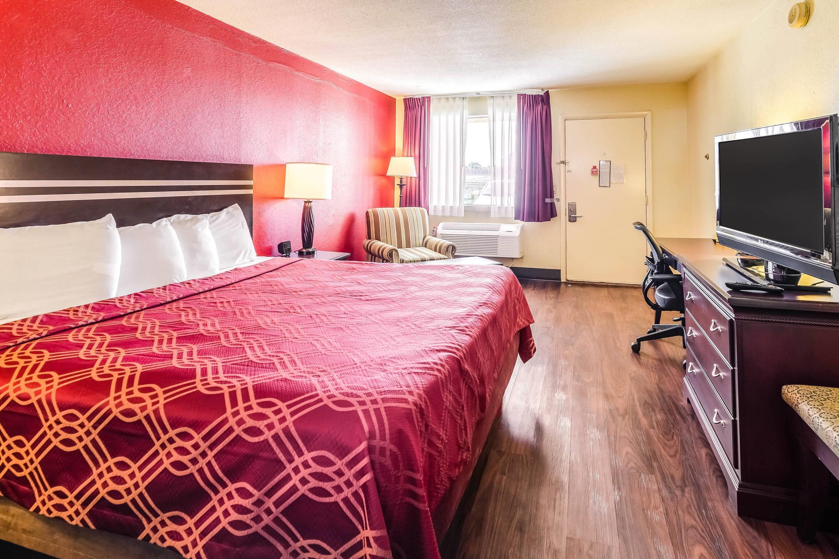 A hotel room with a large bed, a desk with a television, a chair, and a window with curtains.