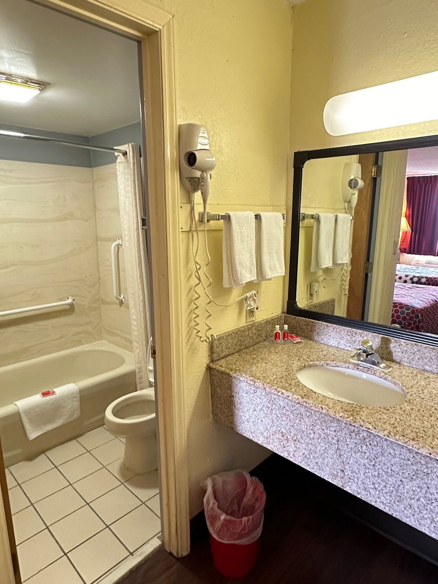 A bathroom with a bathtub, toilet, and sink. There are towels hanging on the wall and a hairdryer on the wall.