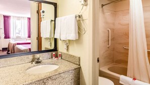A bathroom with a granite countertop, a sink, a mirror, a hairdryer, a shower with a curtain, and a toilet.