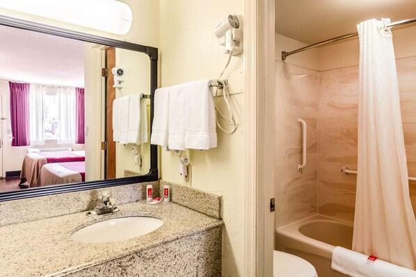 A bathroom with a granite countertop, a sink, a mirror, a hairdryer, a shower with a curtain, and a toilet. - Econo Lodge Christiansburg-Blacksburg I-81 (Christiansburg)