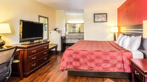 A hotel room with a bed, a desk with a computer, a television, a dresser, and a mirror.
