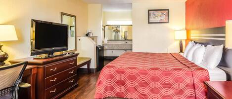 Een hotelkamer met een bed, een bureau met een computer, een televisie, een dressoir en een spiegel.