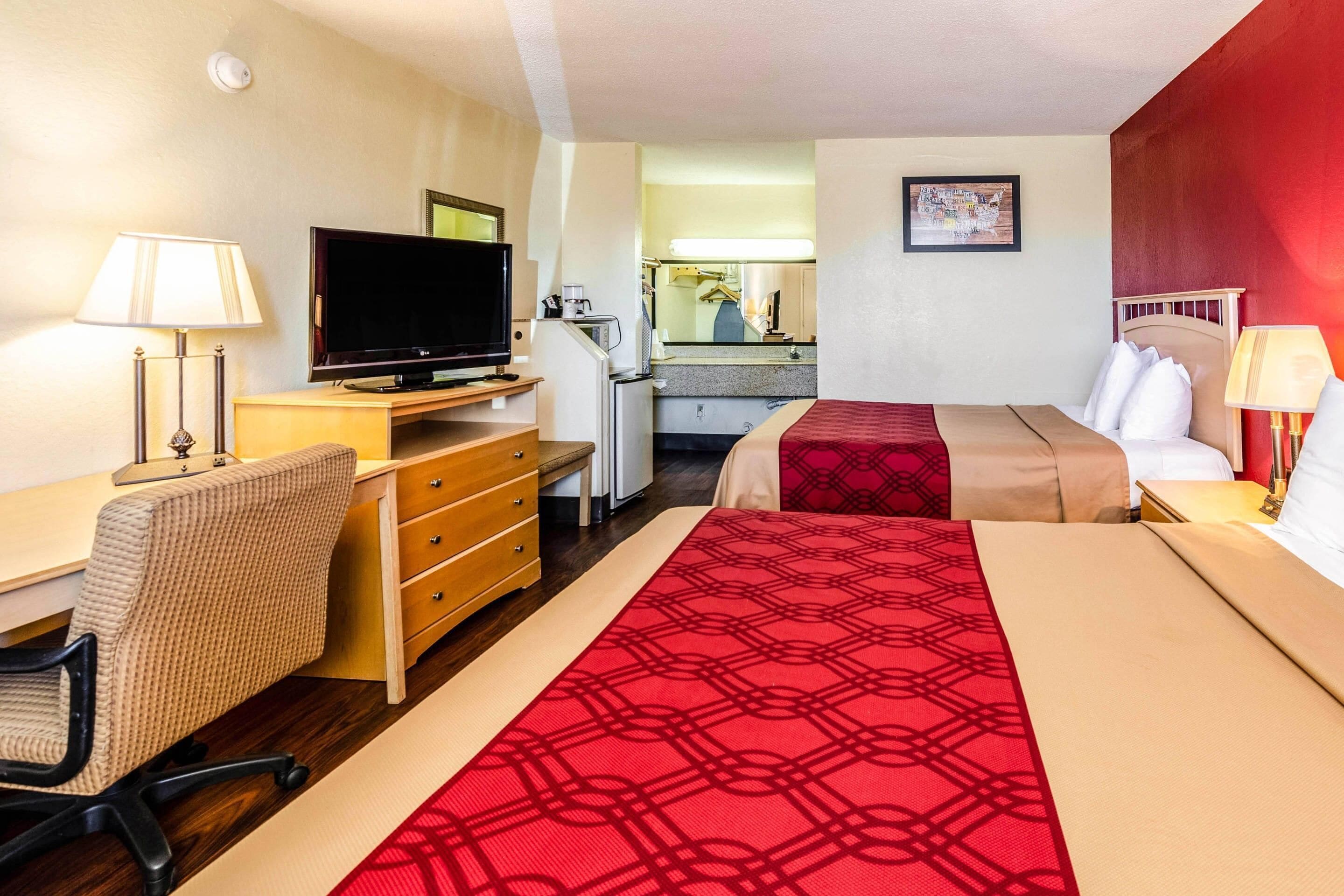 A hotel room with a bed, desk, chair, television, and a small kitchenette.