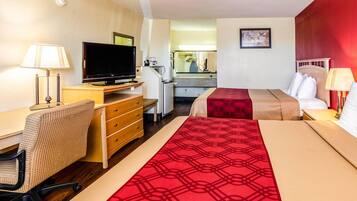 A hotel room with a bed, desk, chair, television, and a small kitchenette.