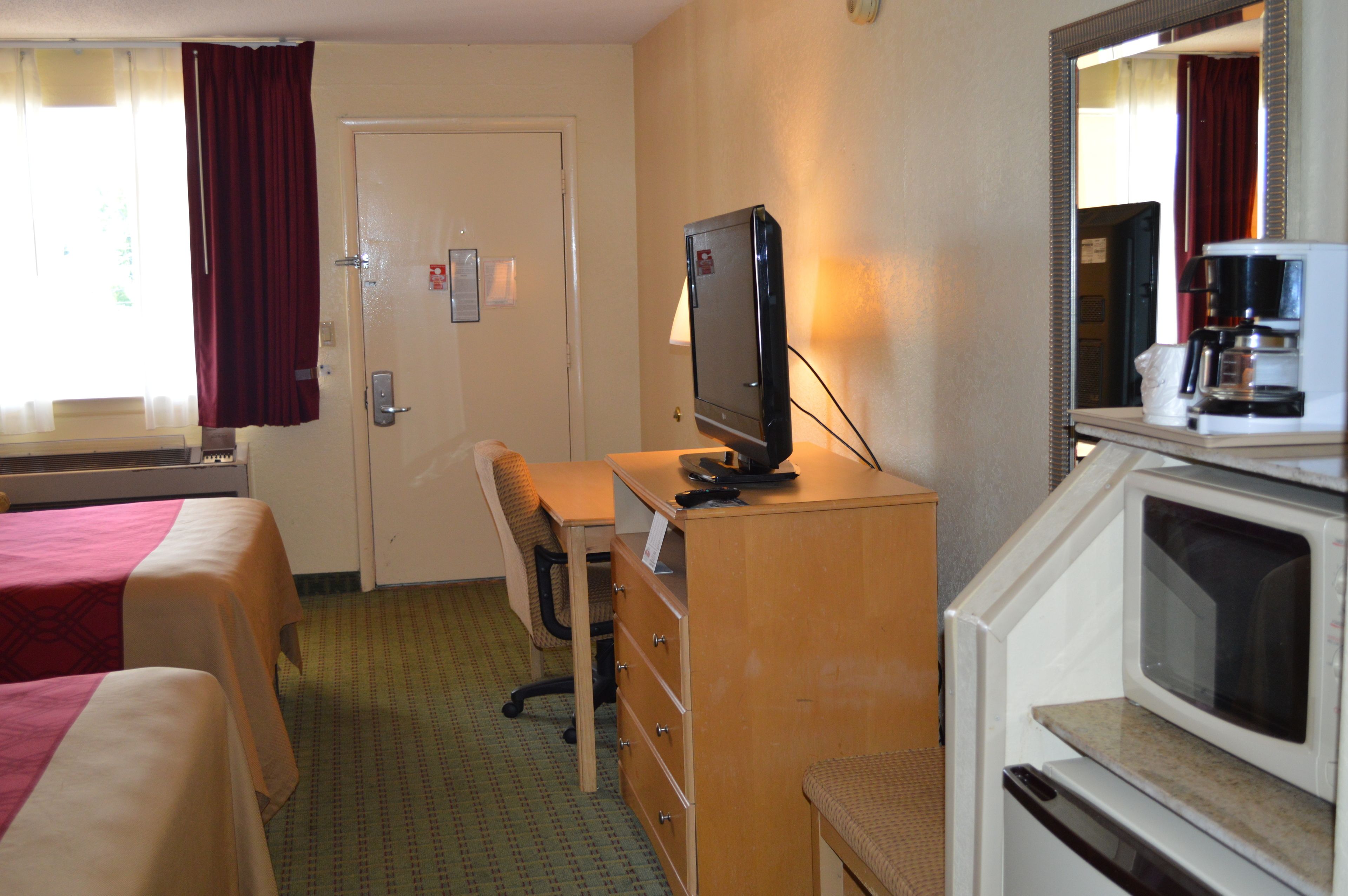 A hotel room with two beds, a desk with a television, a dresser, and a microwave.